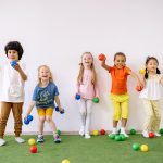 Photo of five pre-school aged children with a variety of racial characteristics, playing with brightly colored balls.
